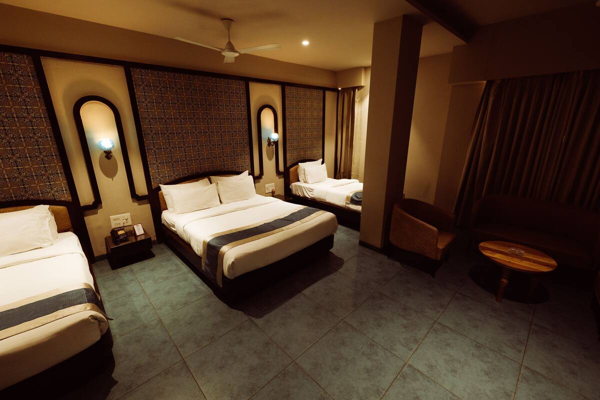 A hotel room with two beds, a small table, a chair, a ceiling fan, and a wall-mounted light fixture.