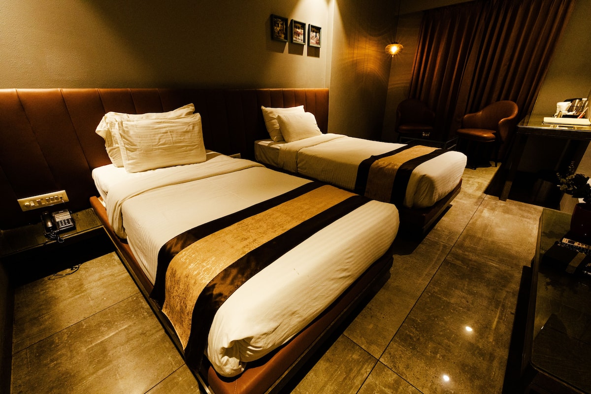 A hotel room with two beds, a desk, a chair, and a phone on the nightstand.