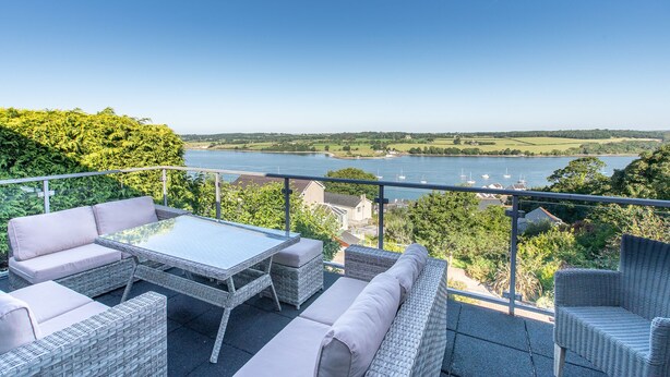 A terrace with wicker furniture, a glass table, and a view of a river with boats. - Beautiful family home with fantastic views over the Menai straits (Y Felinheli)