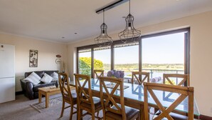 A dining area with a glass table and wooden chairs, a sofa, and a view of a lake through large windows. - Beautiful family home with fantastic views over the Menai straits (Y Felinheli)