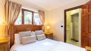 A bedroom with a wooden headboard, a large bed with white linens, a bedside table with a lamp, and a view of a shower area through an open door. - Beautiful family home with fantastic views over the Menai straits (Y Felinheli)