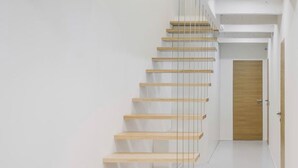A modern staircase with glass railings and wooden steps leading to a door. - Via del Centro (Oristano)