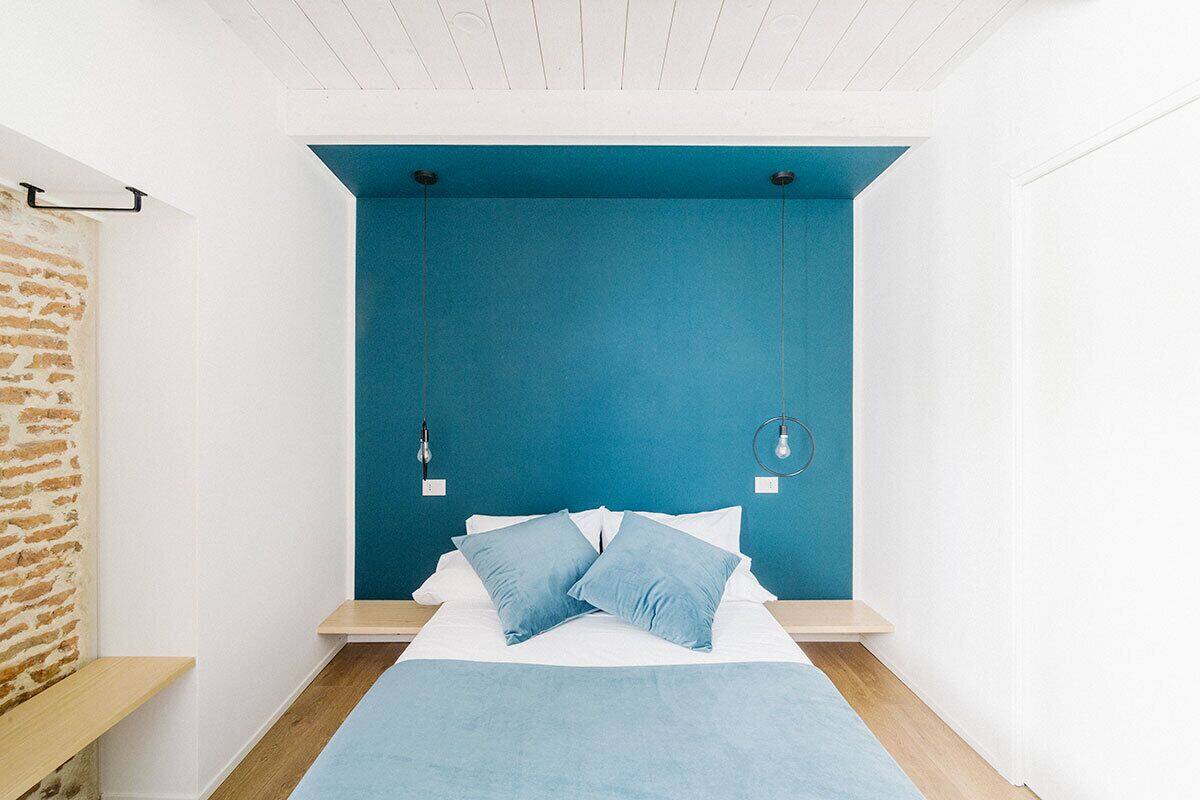 A bedroom with a blue accent wall, a bed with blue bedding, and a hanging light fixture.