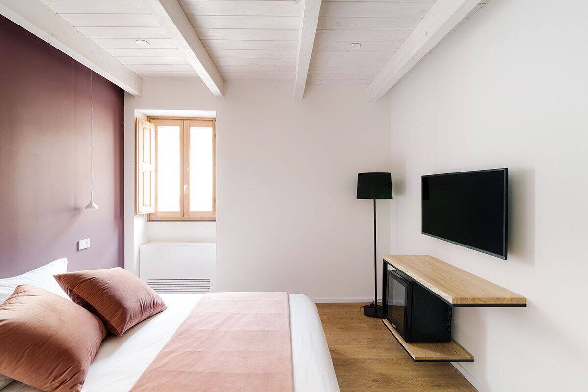 A modern bedroom with a bed, a TV mounted on the wall, and a window providing natural light.