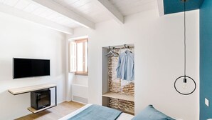 A modern bedroom with a bed, a TV, a hanging light fixture, and a brick wall closet. - Via del Centro (Oristano)