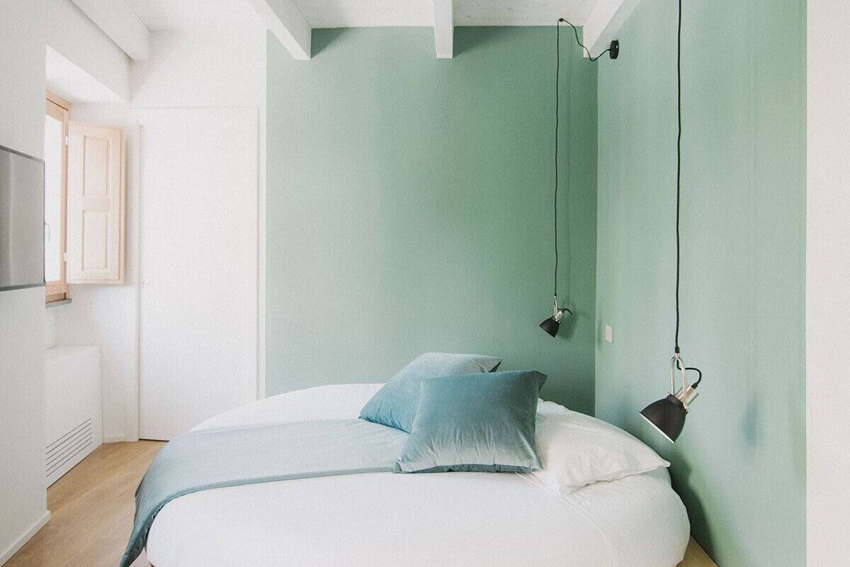 A circular bed with a wooden frame, a light green wall, and a hanging lamp.