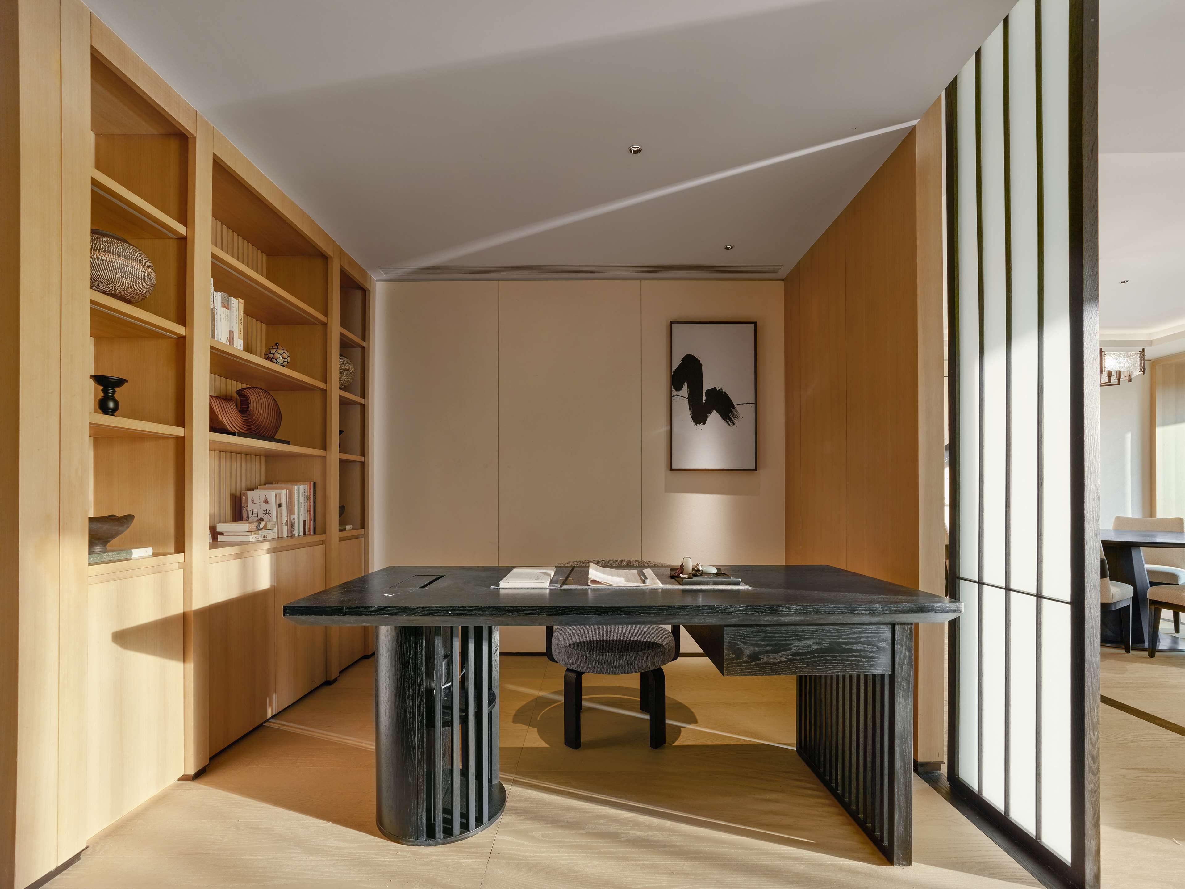 A modern dining area with a dark wooden table, a chair, and a bookshelf filled with books and decorative items.