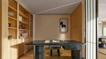 A modern dining area with a dark wooden table, a chair, and a bookshelf filled with books and decorative items.