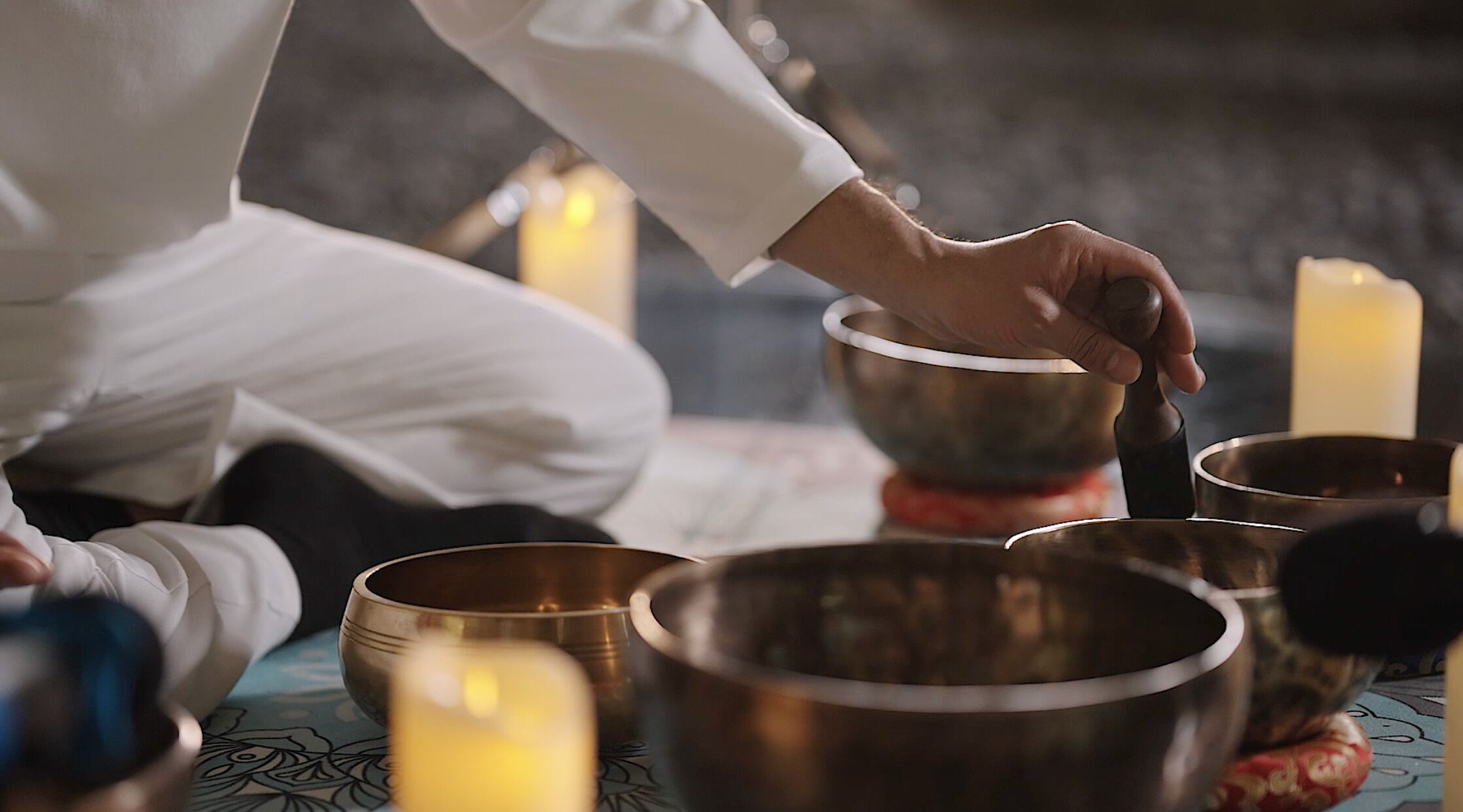 A person sitting on a patterned mat, holding a singing bowl.
