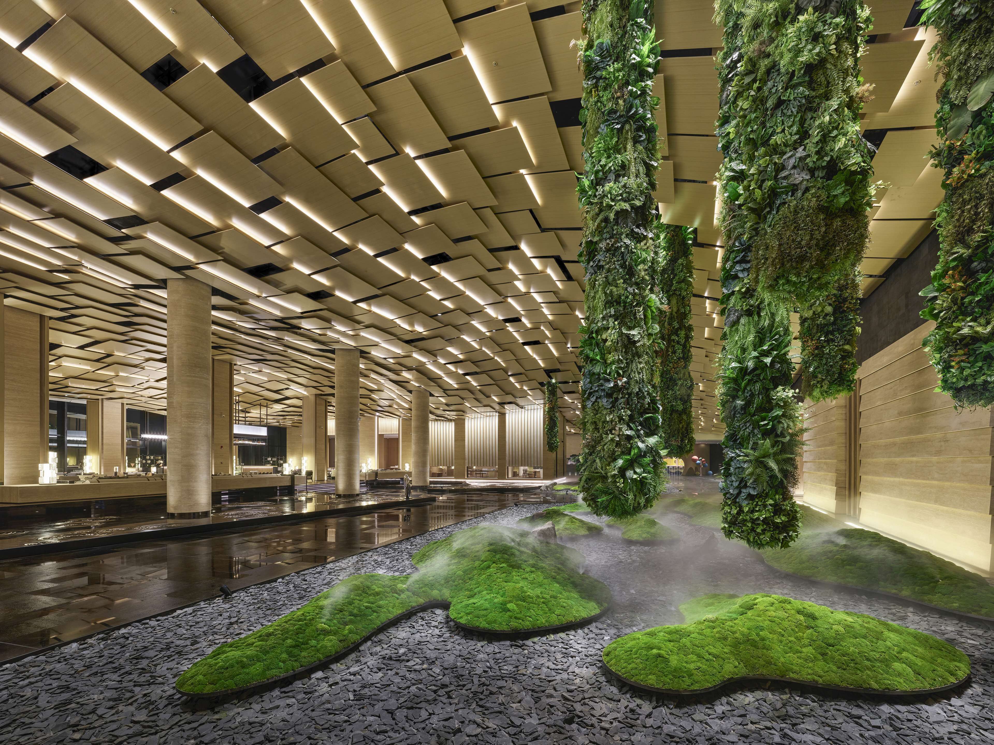 Un vestíbulo moderno con techo alto, jardines verticales verdes y una fuente central.