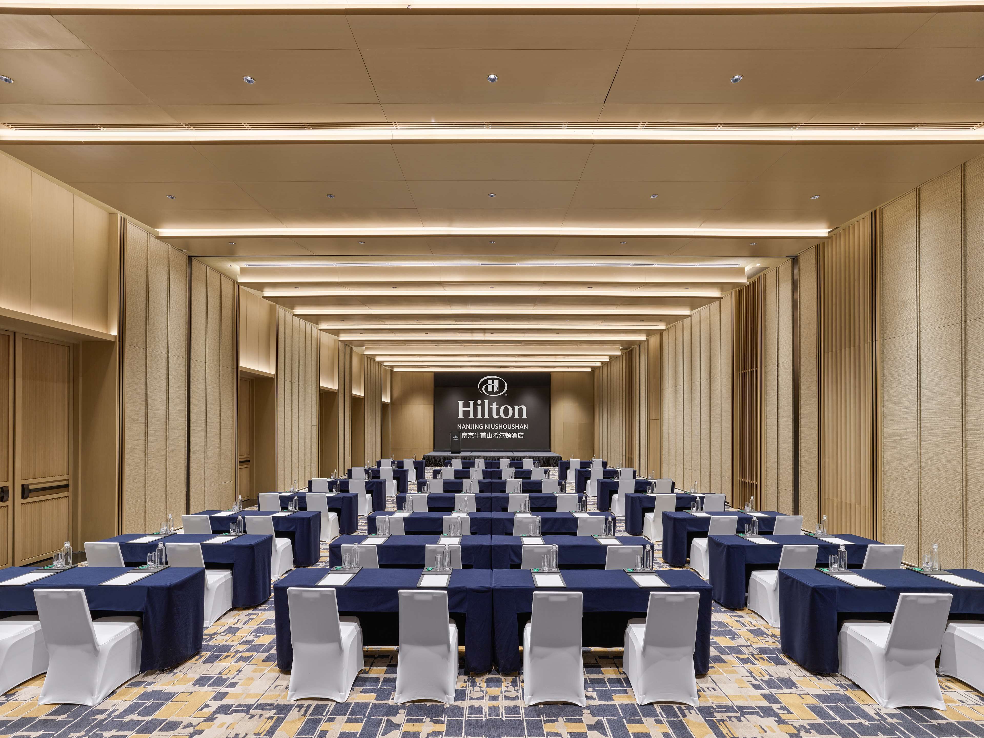 A conference room with multiple tables and chairs, a large sign with the Hilton logo, and a patterned carpet.
