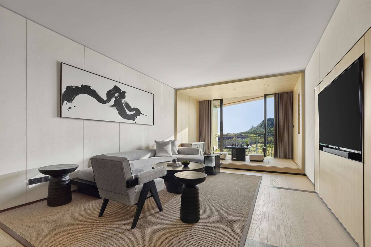 A modern hotel room with a sofa, armchairs, a coffee table, and a large TV.