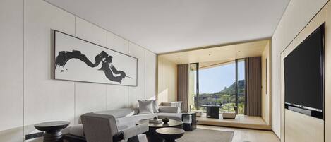 A modern hotel room with a sofa, armchairs, a coffee table, and a large TV.