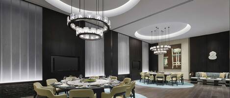 A modern dining area with a round table, multiple chairs, and two chandeliers.