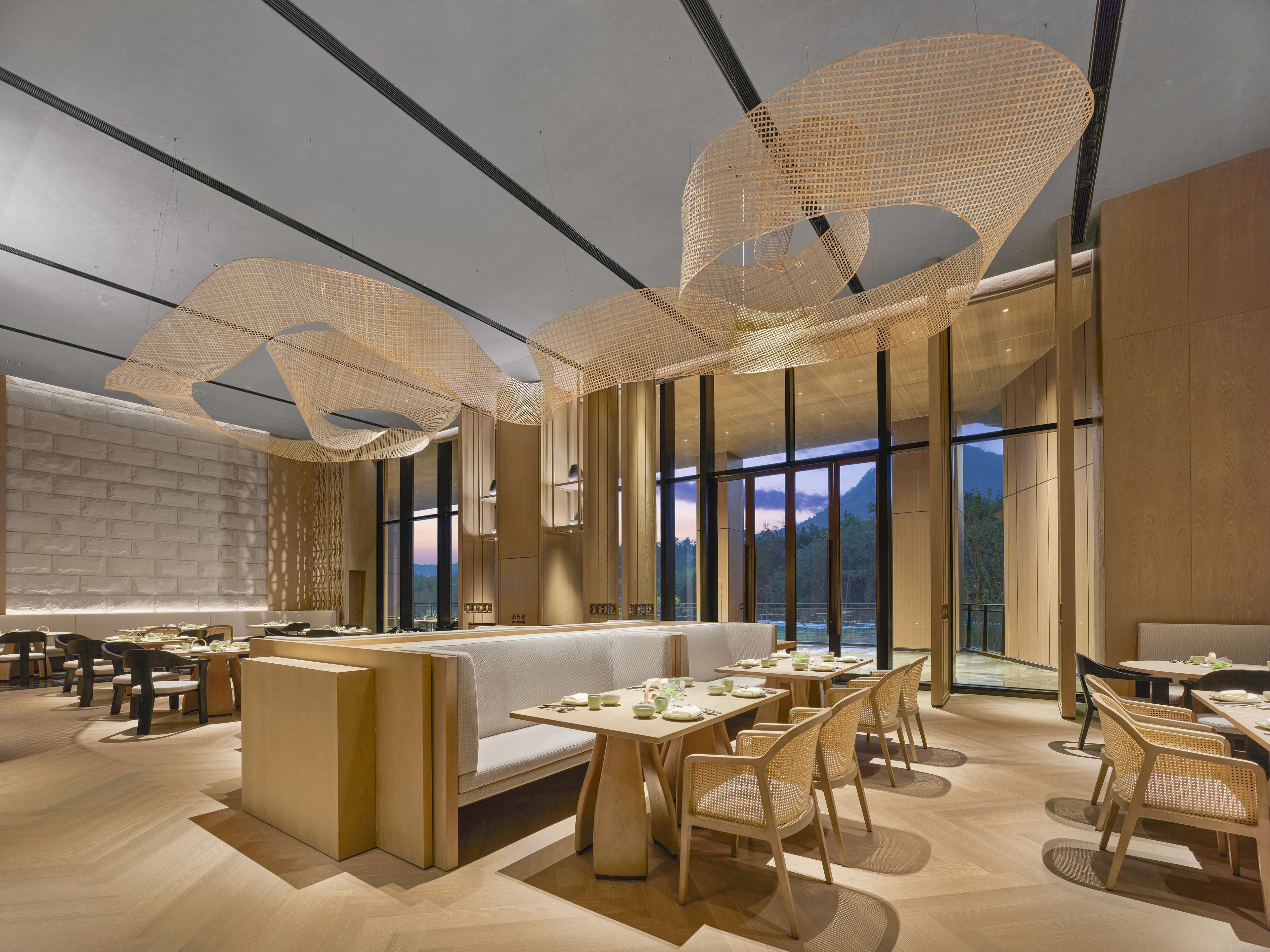Interior modern d'un restaurant amb sostres alts, grans finestres i vistes a les muntanyes.