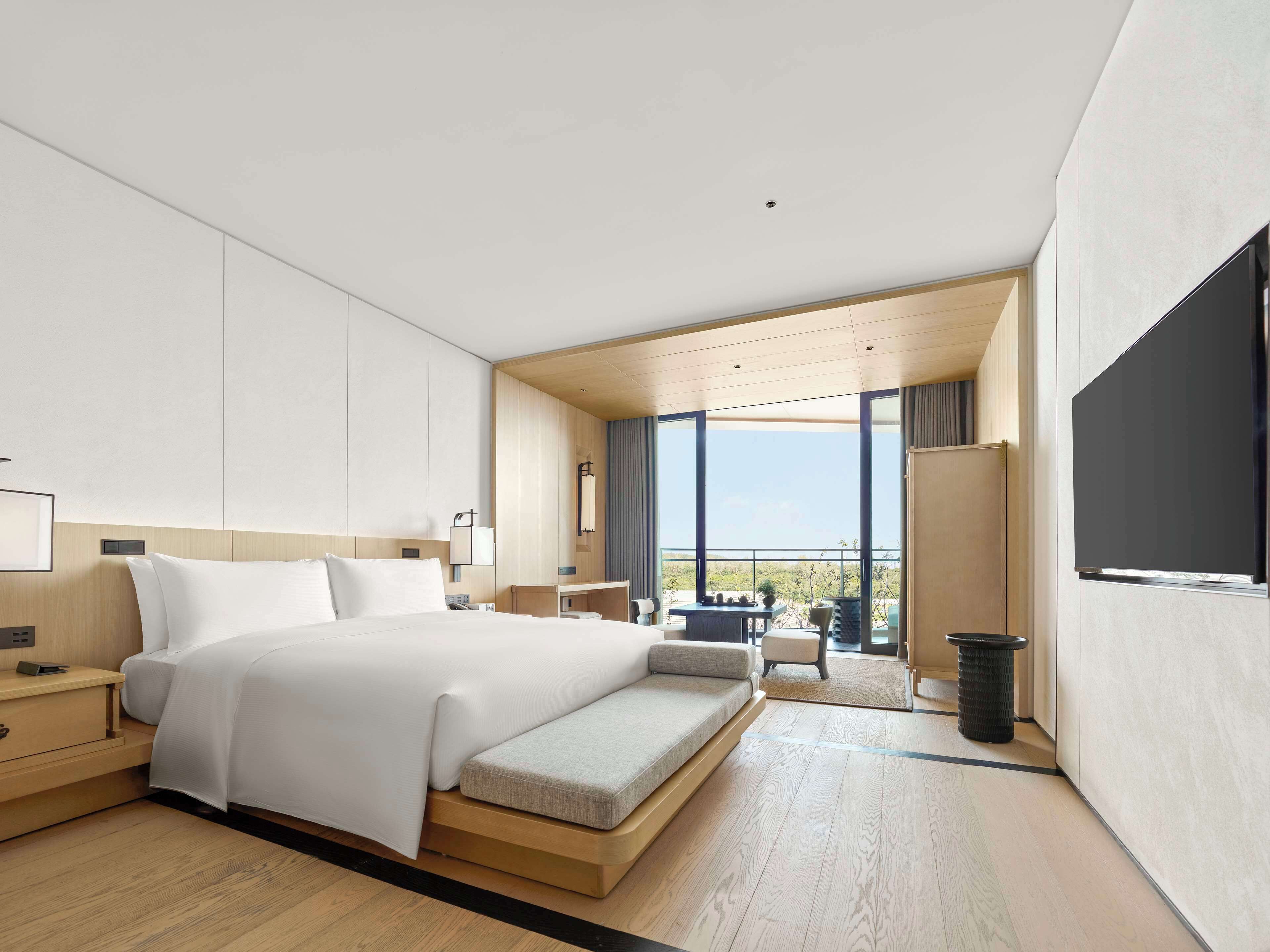 Una habitación de hotel moderna con una cama grande, un área de descanso y un balcón con vistas.