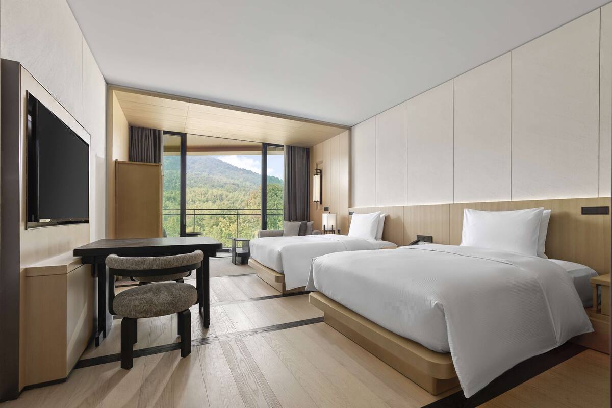 A modern hotel room with two beds, a desk, and a chair.