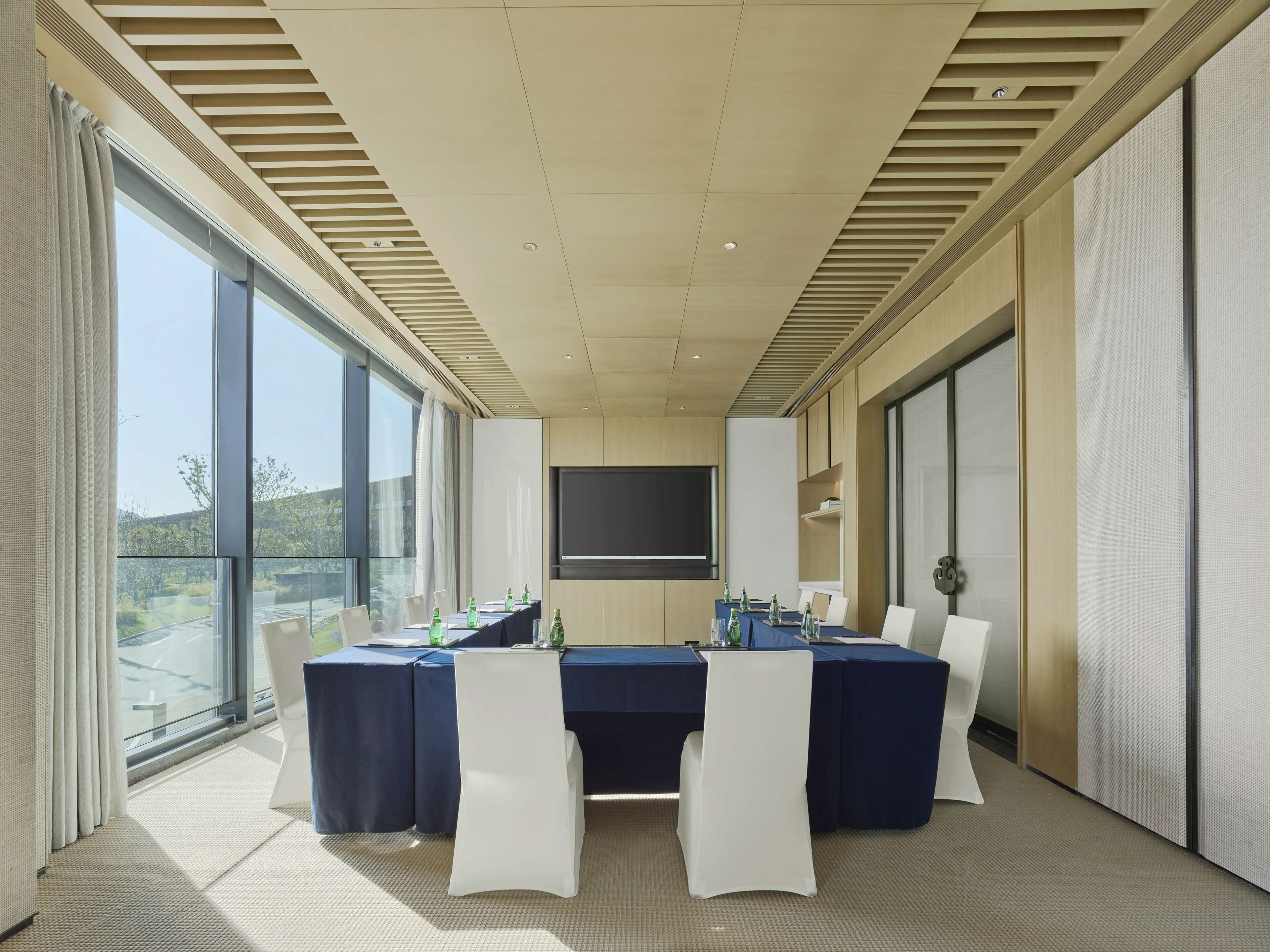 A conference room with a long table, white chairs, and a large screen.