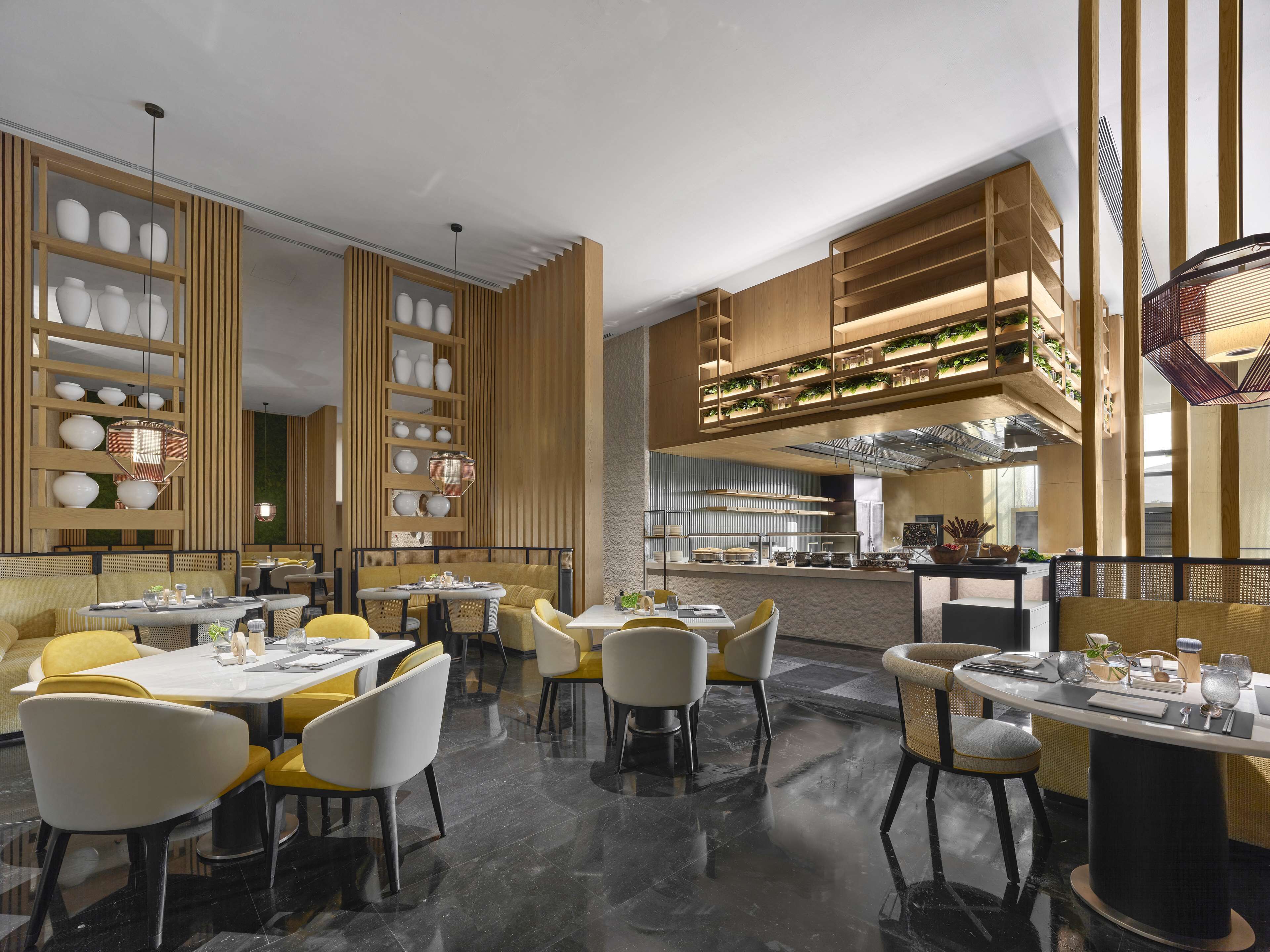 A modern restaurant interior with high ceilings, wooden paneling, and a central kitchen area.