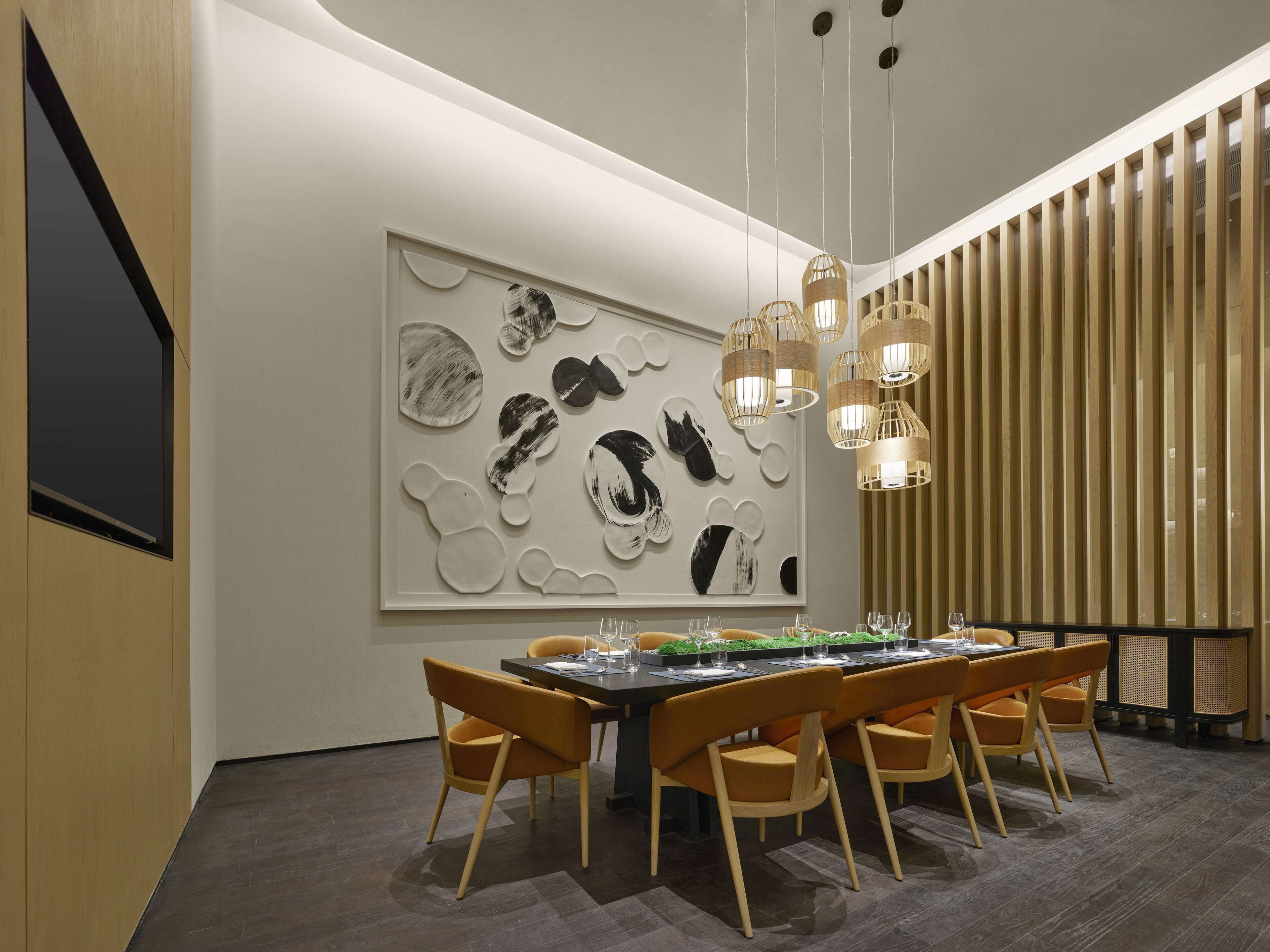 A modern dining area with a large abstract art piece on the wall, a long table with chairs, and hanging pendant lights.