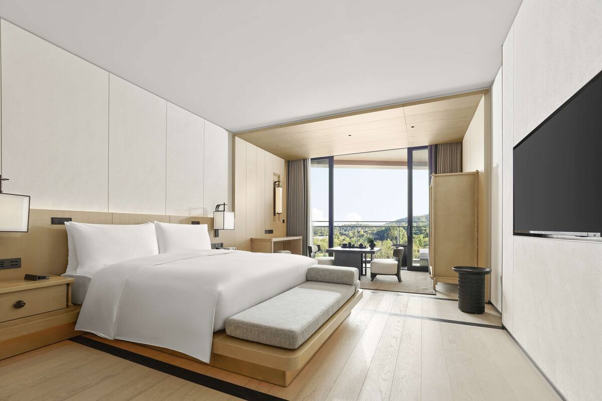 A modern hotel room with a large bed, a desk, and a view of the outdoors.