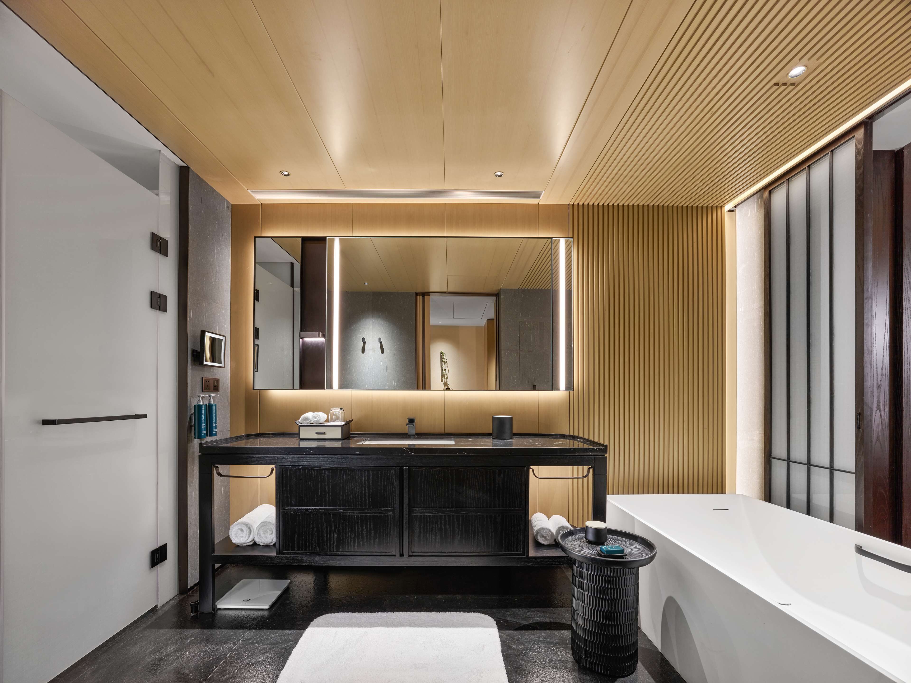 Un bagno moderno con un grande specchio, un mobile lavabo nero, una vasca da bagno e un lavandino bianco.