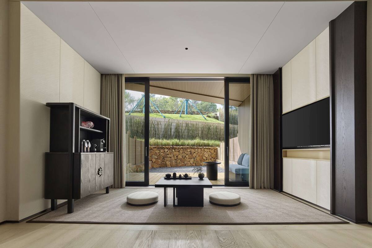 A modern living room with a large sliding glass door leading to an outdoor area, a built-in entertainment unit, and a minimalist design.