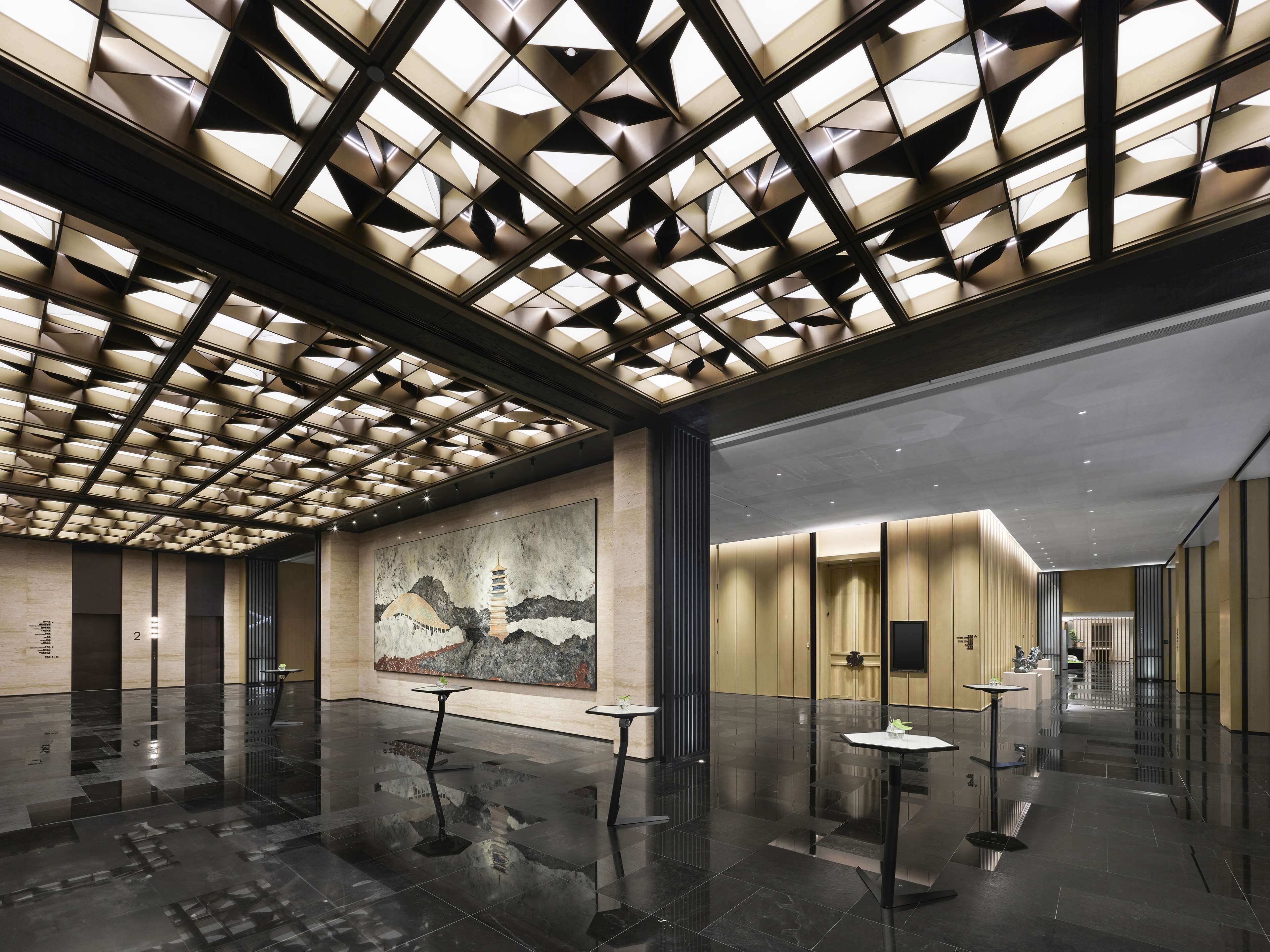Un hall d’entrée moderne avec un plafond au design géométrique, une grande fresque murale et un sol épuré et réfléchissant.