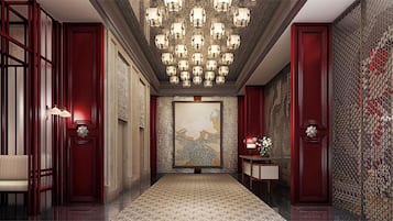 A hallway with a patterned carpet, a chandelier, and a painting on the wall.