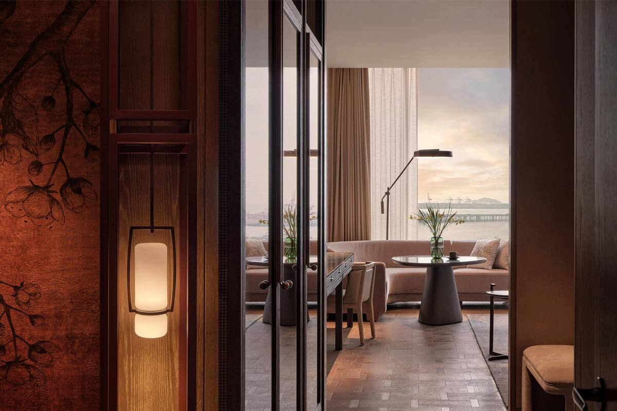 A modern living room with a sofa, chairs, a coffee table, and a view of a cityscape through large windows.