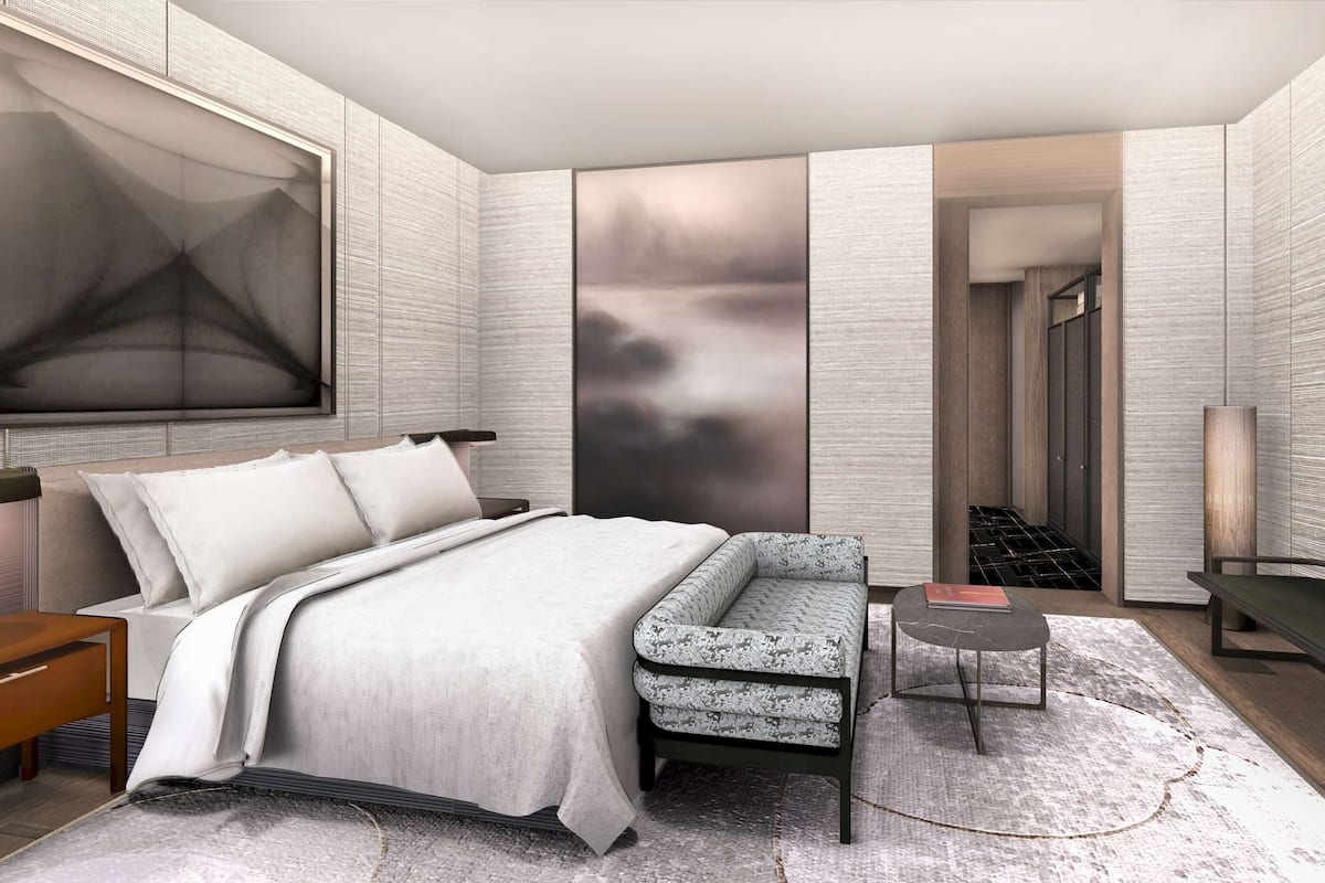A modern bedroom with a bed, seating area, TV, and a large artwork on the wall.