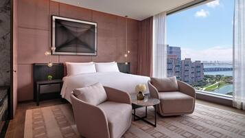 A modern hotel room with a large bed, two armchairs, a small table, and a city view.