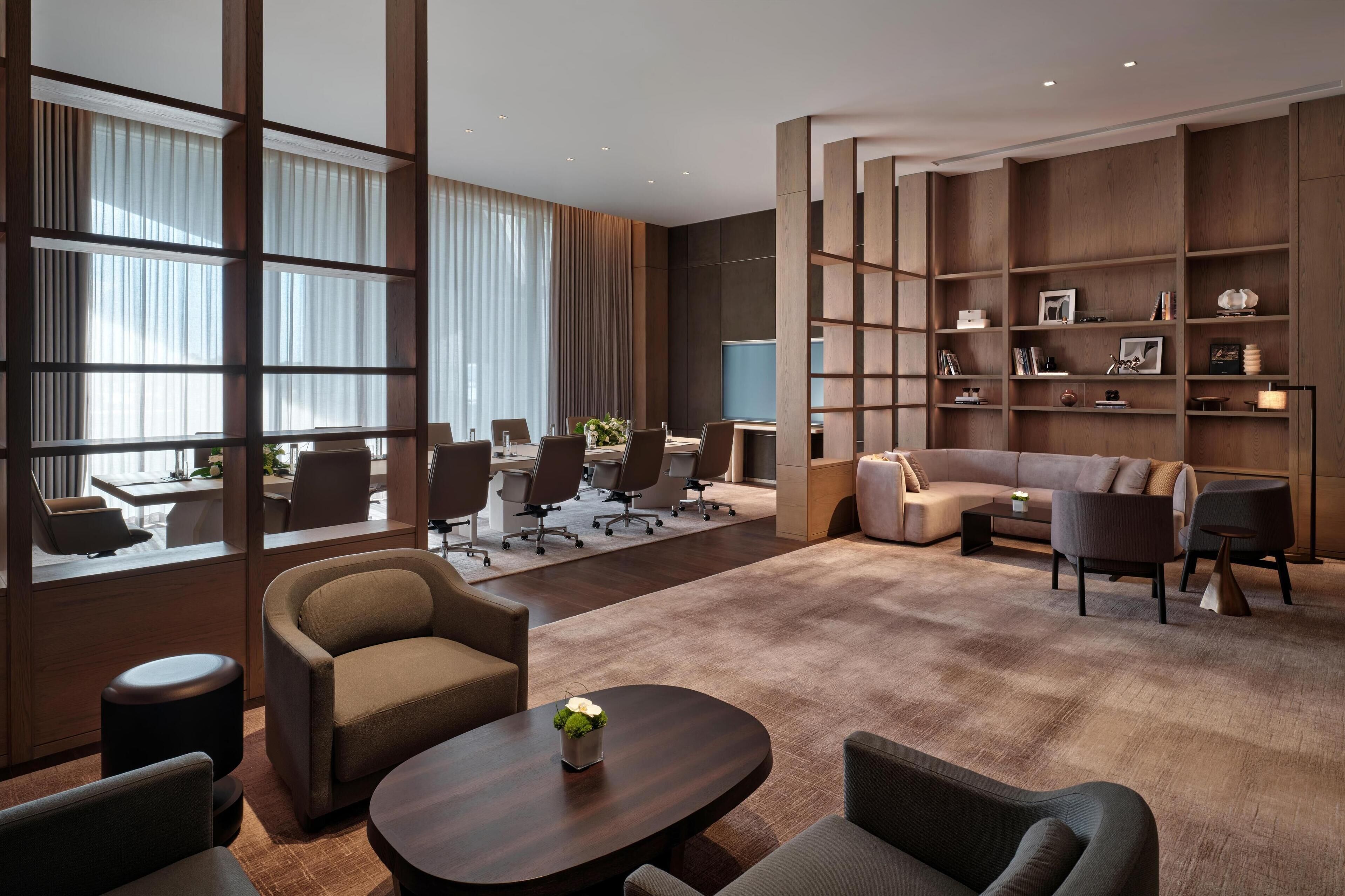A modern hotel lobby with a conference room, seating area, and a bookshelf.