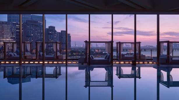 Habitación de hotel moderna con un amplio ventanal que ofrece vistas a la ciudad al anochecer.