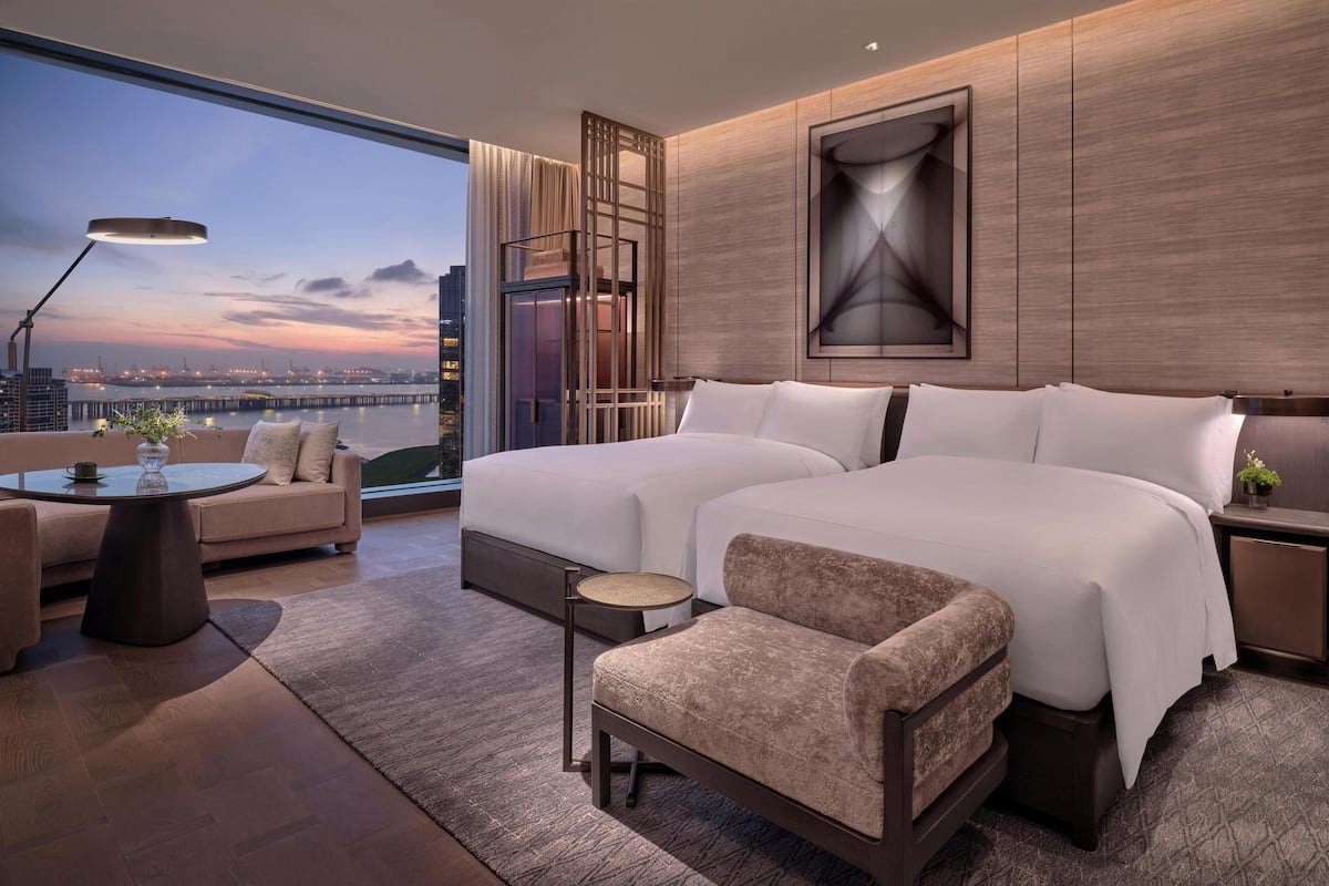 A modern hotel room with a large bed, a sofa, a small table, and a view of the cityscape.