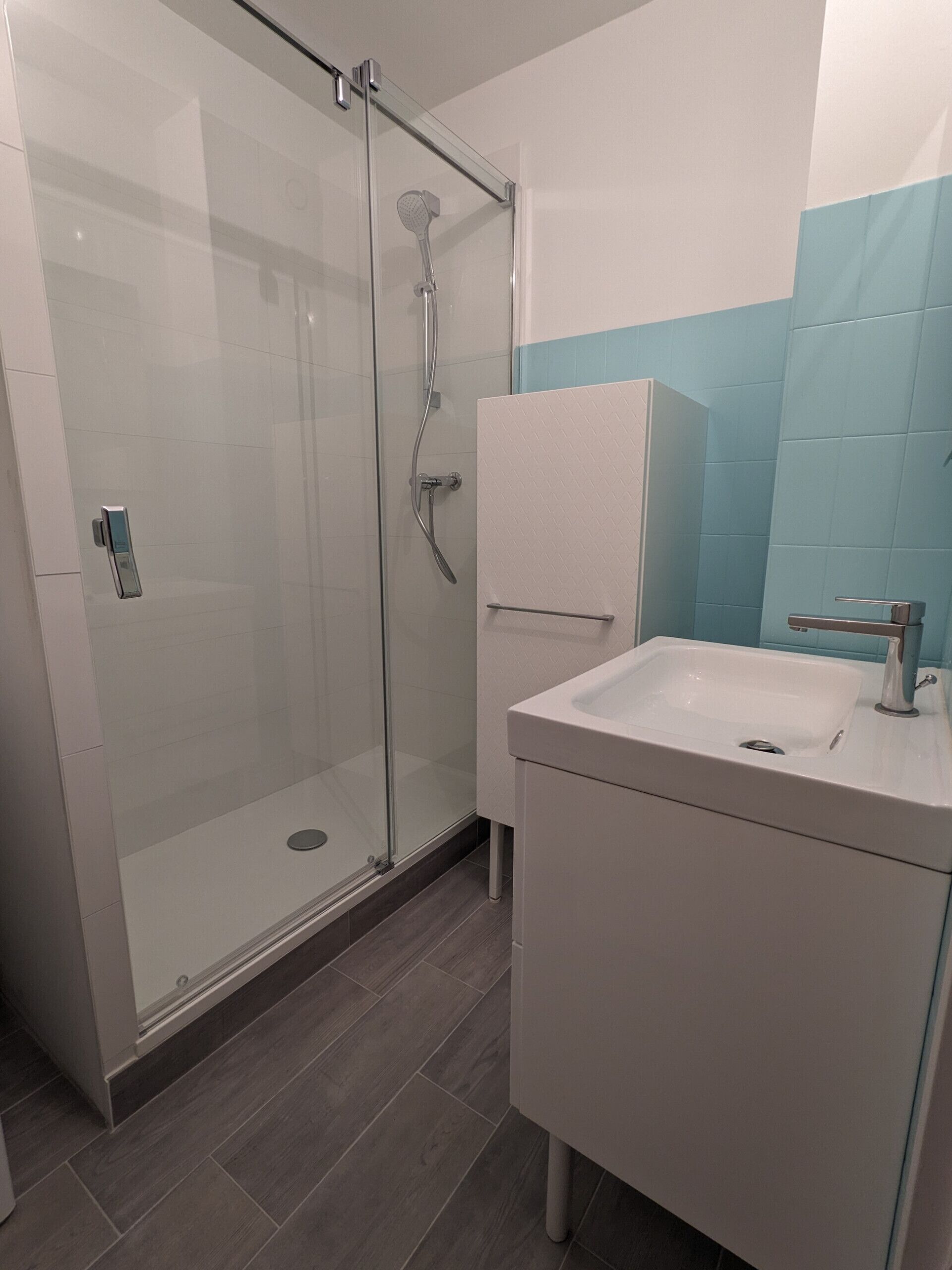 Un baño moderno con cabina de ducha de vidrio, un lavabo blanco y pared revestida con azulejos azules.