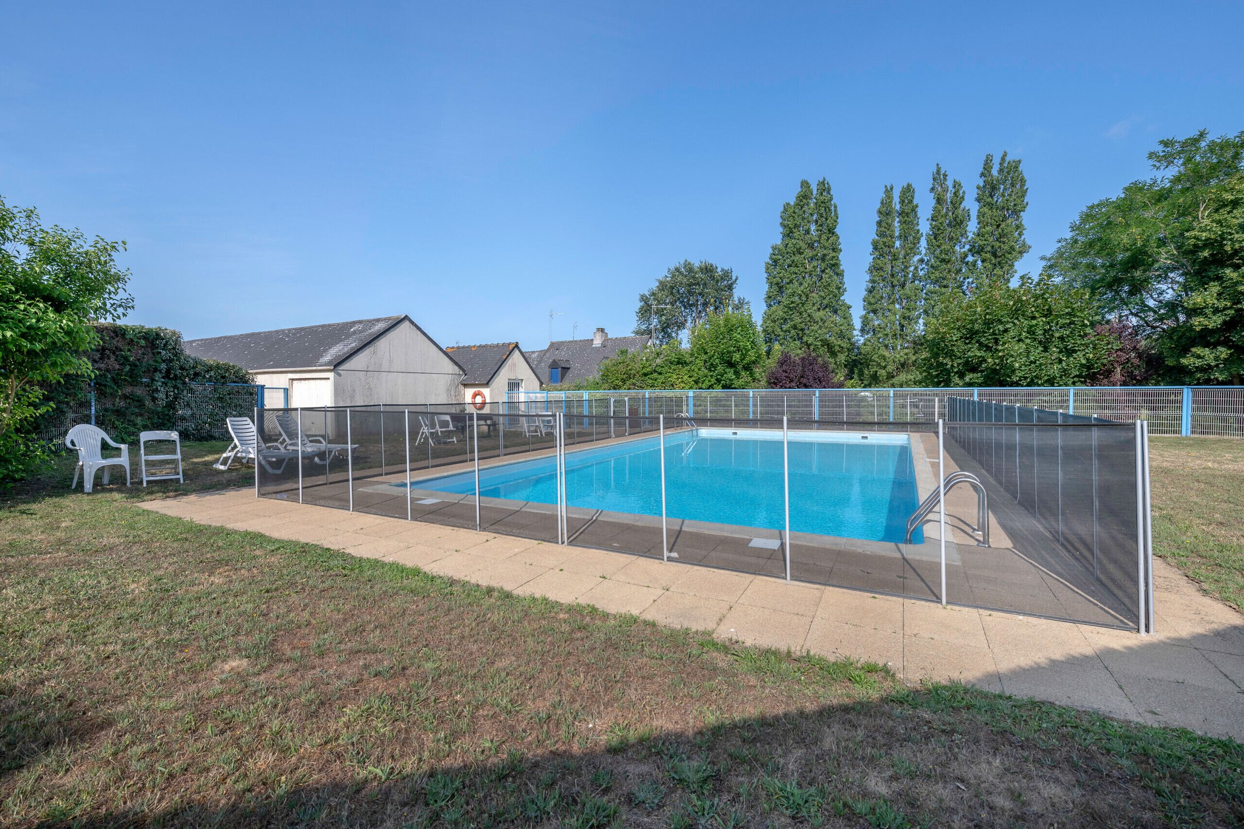 A rectangular swimming pool with a metal fence, surrounded by a grassy area and trees.