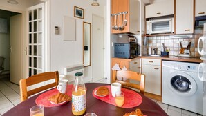 Ett kompakt kök med tvättmaskin, mikrovågsugn och en matplats med ett bord dukat för frukost.