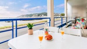 Ett bord med en croissant, en flaska juice och ett glas apelsinjuice på en balkong med utsikt över kusten.