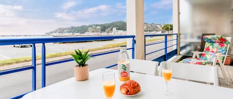 Una mesa con un croissant, una botella de jugo y un vaso de jugo de naranja en un balcón con vistas al mar.