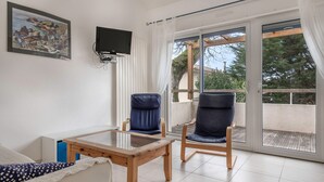 Una habitación con cama, una mesa, dos sillas, un televisor y un ventanal corredizo a un espacio exterior.
