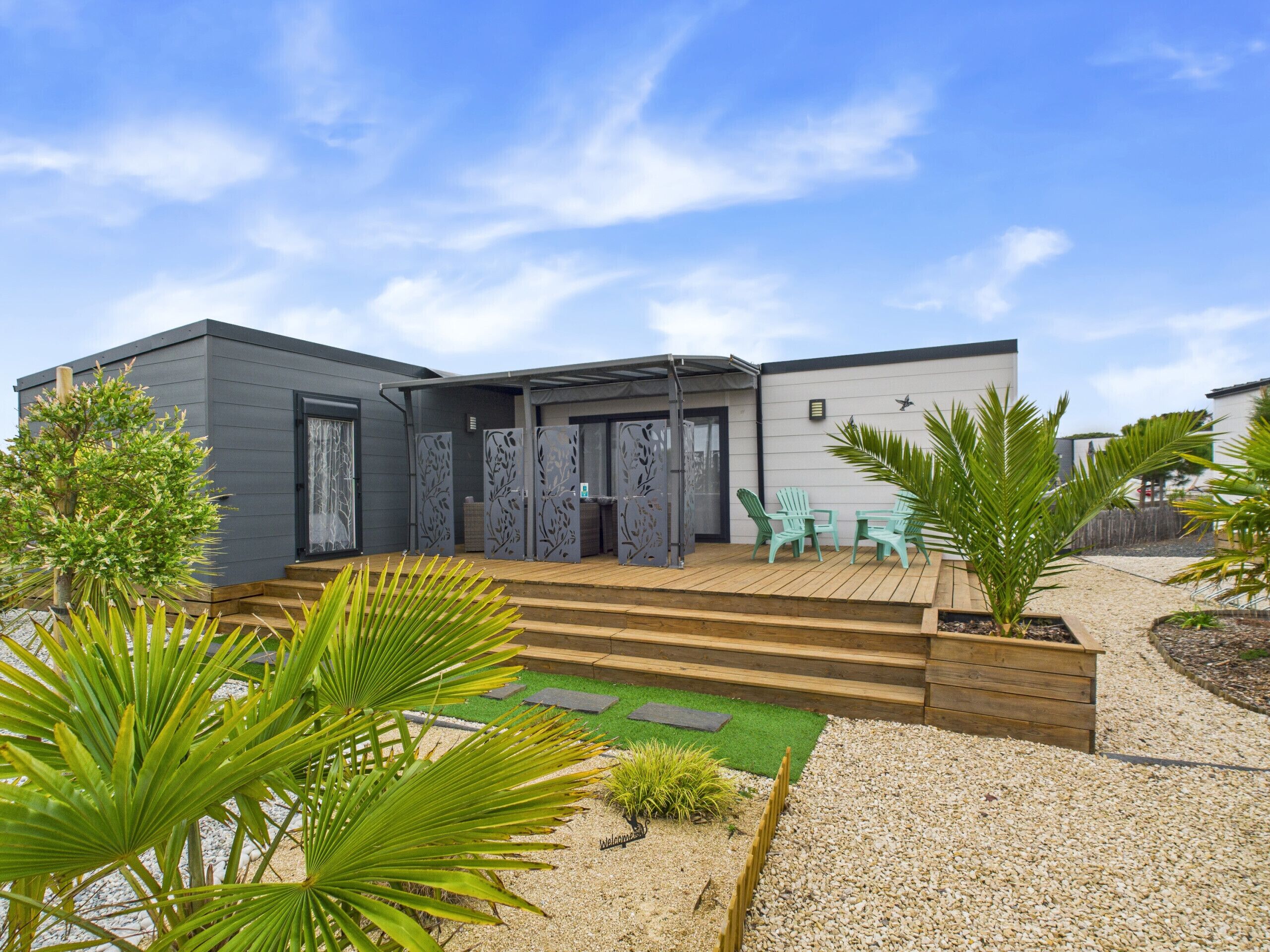Une maison moderne avec un patio, deux chaises vertes et un petit jardin.