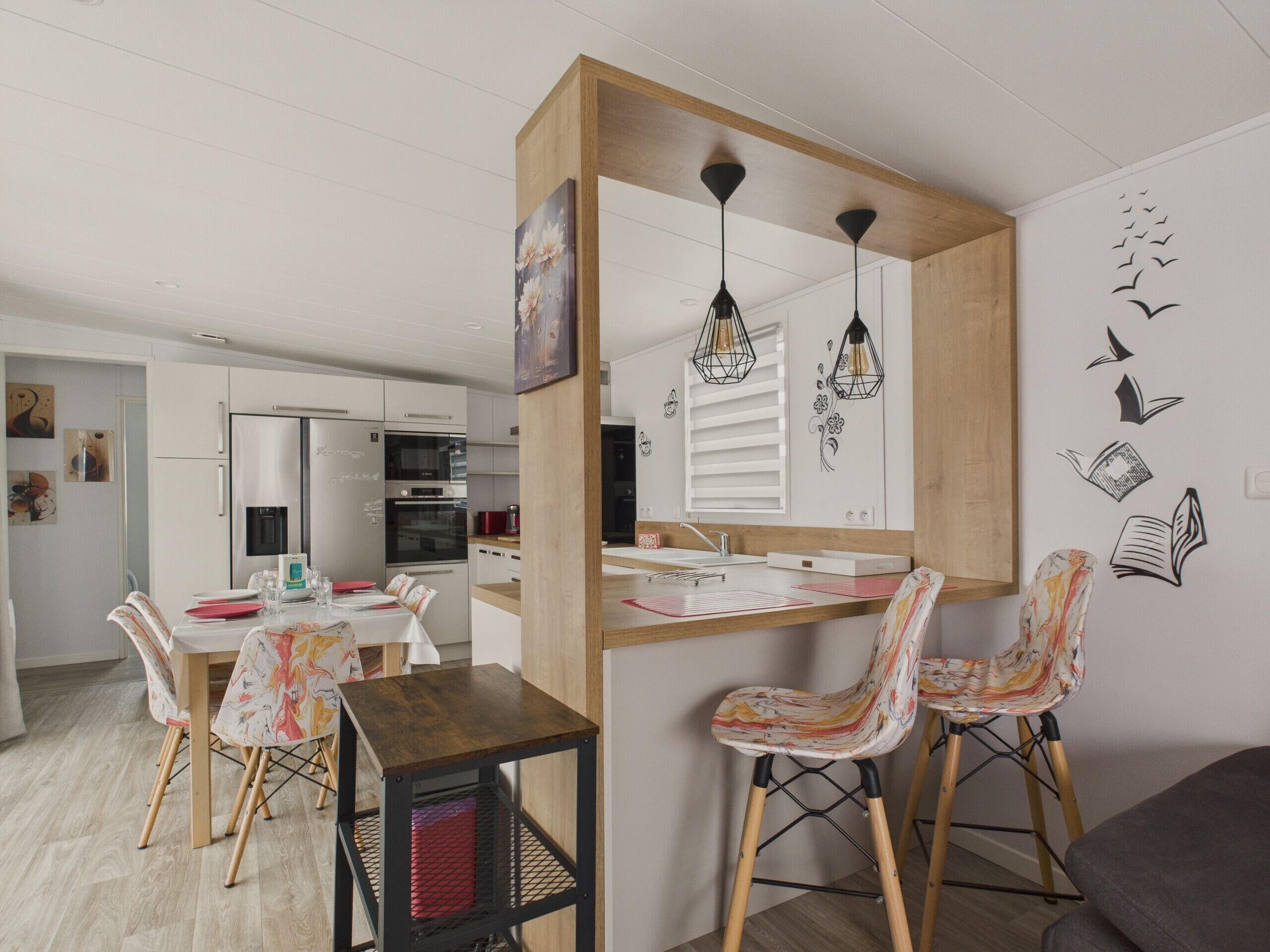 Une cuisine moderne avec des armoires blanches, un îlot central en bois et des luminaires suspendus. On y trouve également un coin repas avec des chaises à motifs et une table.