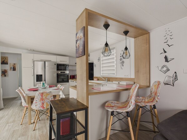 A modern kitchen with white cabinets, a wooden island, and pendant lights. There is a dining area with patterned chairs and a table.