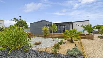 Een modern huis met een grijze gevel, een houten terras en een kiezelgaard met diverse planten.