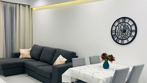 A modern living room with a sectional sofa, a dining table with chairs, and a wall clock. - Central Cozy Located Apt (Msida)