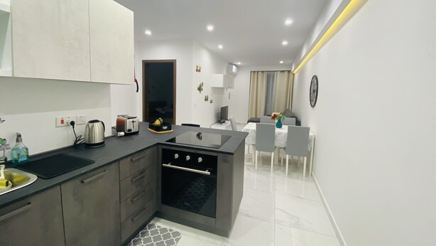 A modern kitchen with a built-in oven, a dining area with a white table and chairs, and a small island with a sink. - Central Cozy Located Apt (Msida)