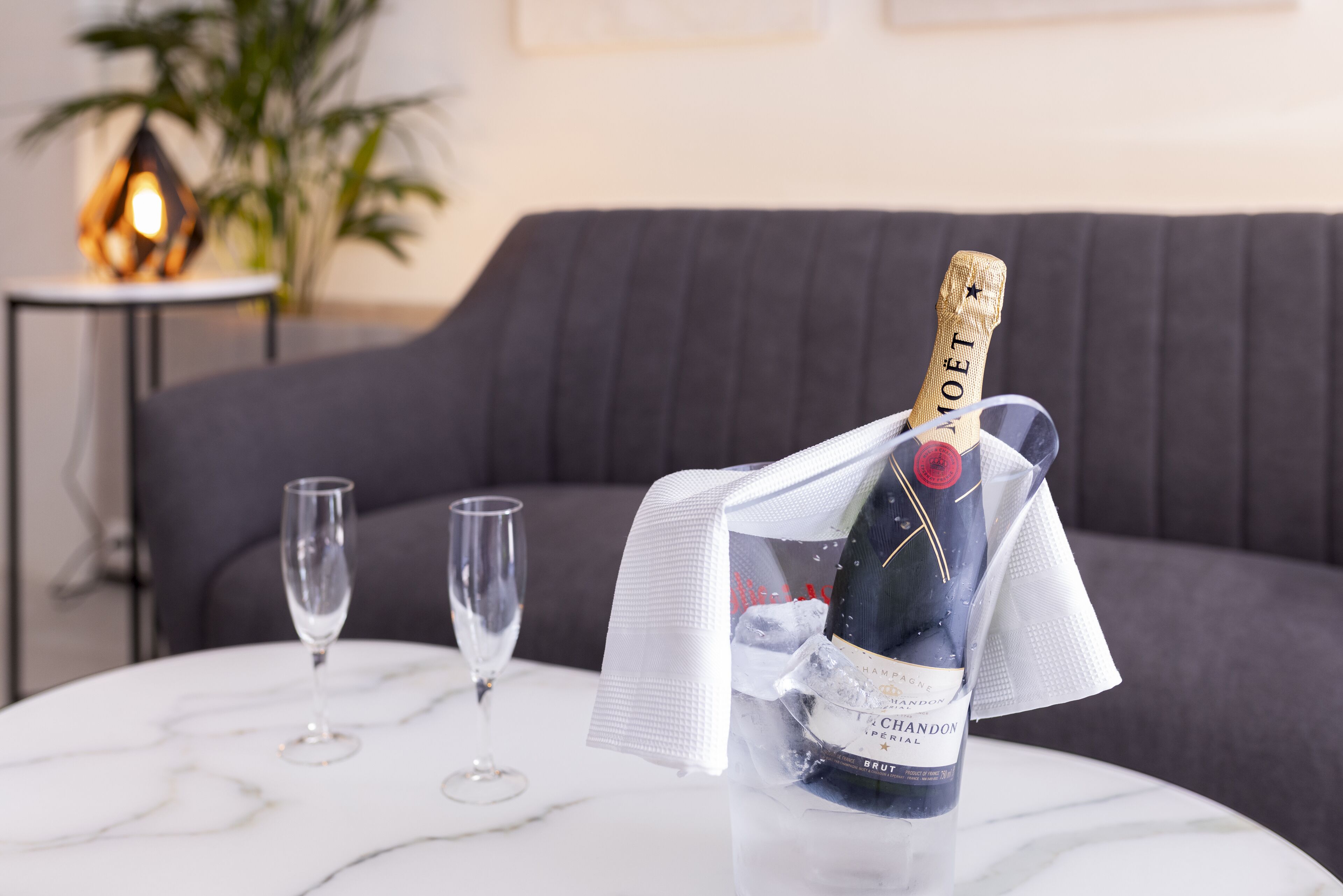 A bottle of champagne on a white marble table with two glasses.