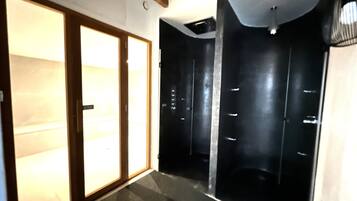 Un couloir doté d’une porte coulissante qui donne sur une pièce au sol et aux murs sombres, et dont le plafond est orné d’un luminaire.