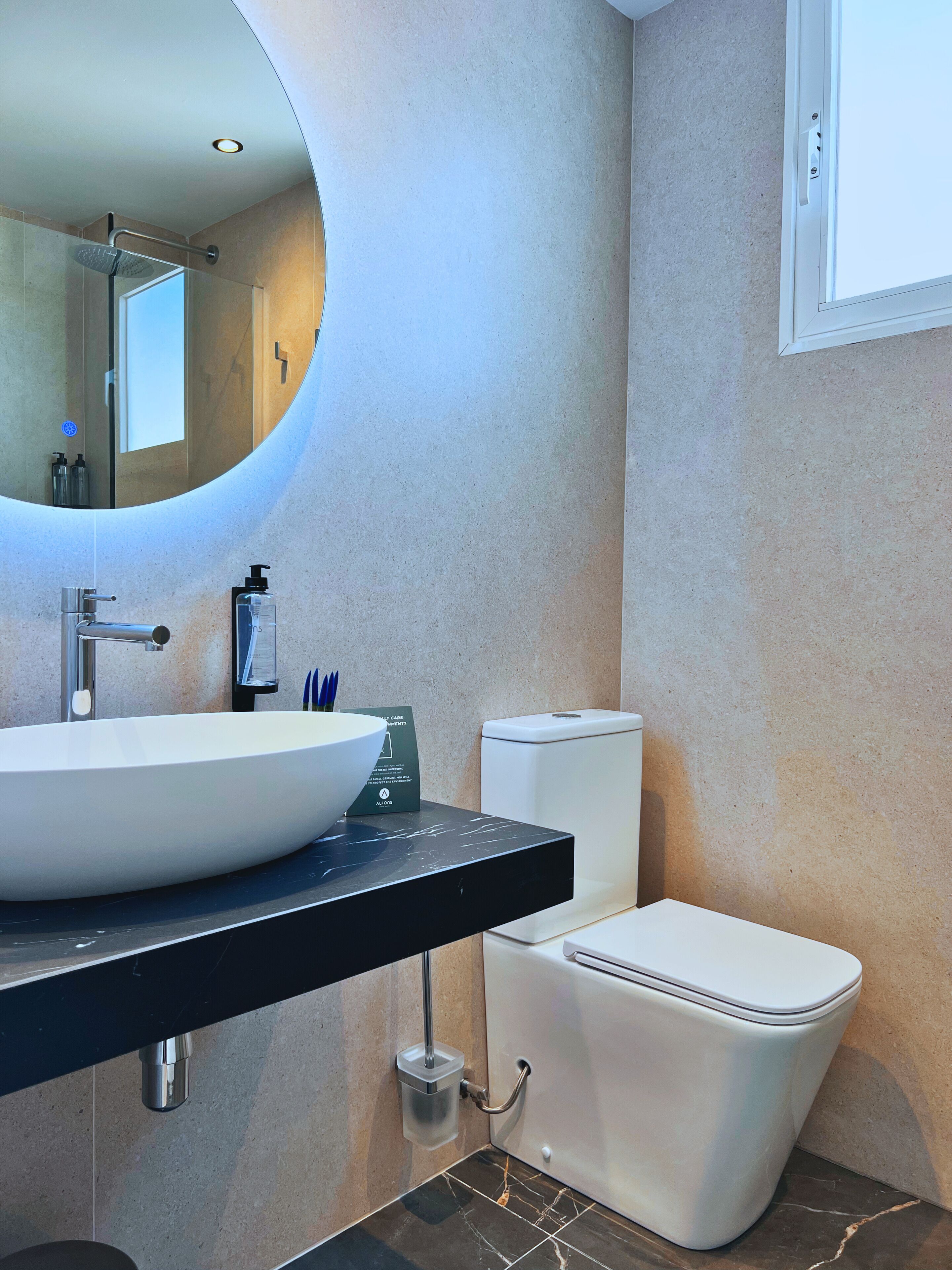 A modern bathroom with a round mirror, a white sink, and a toilet.